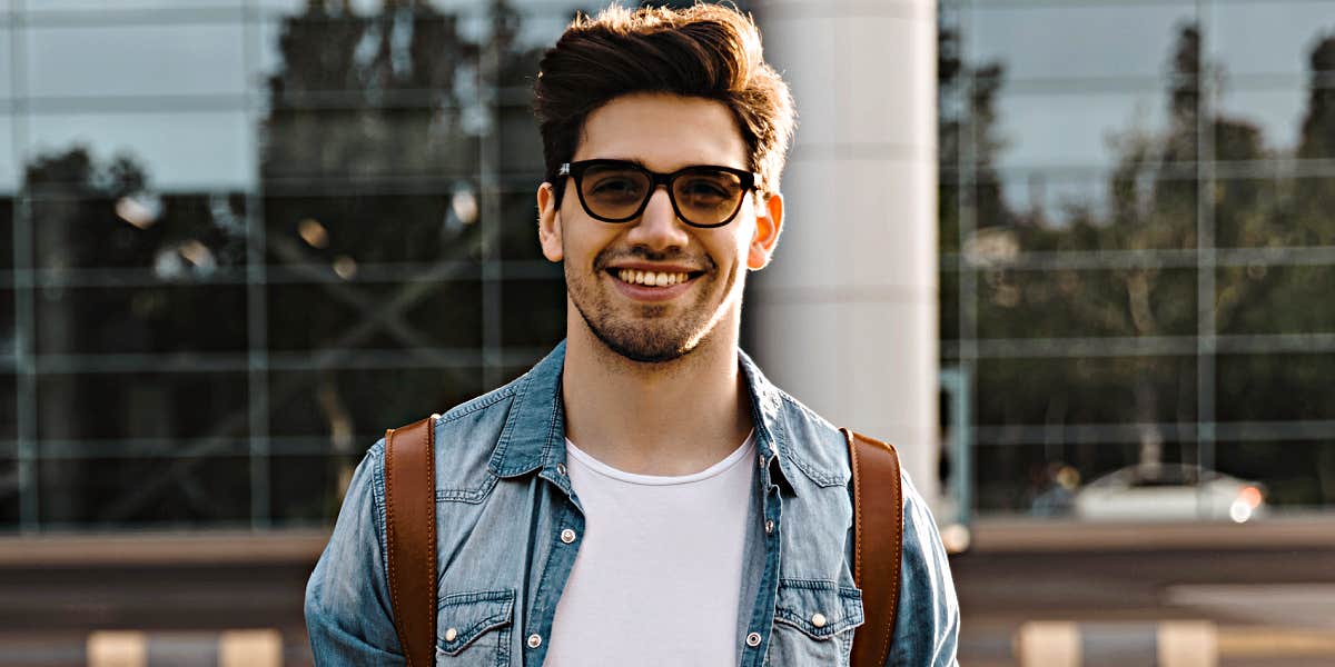 young man with dark hair and glasses smiles at camera