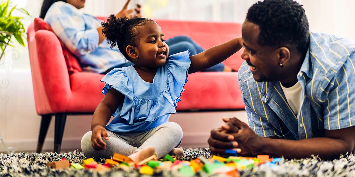 dad laying on floor with young daughter playing with blocks