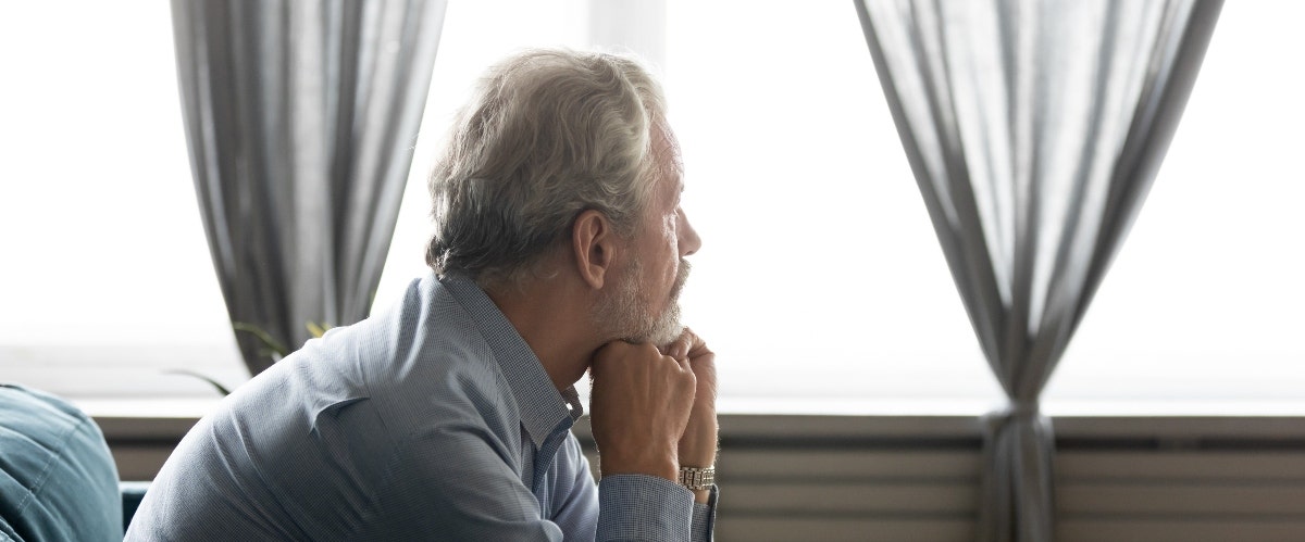 middle aged man sitting on couch looking out window