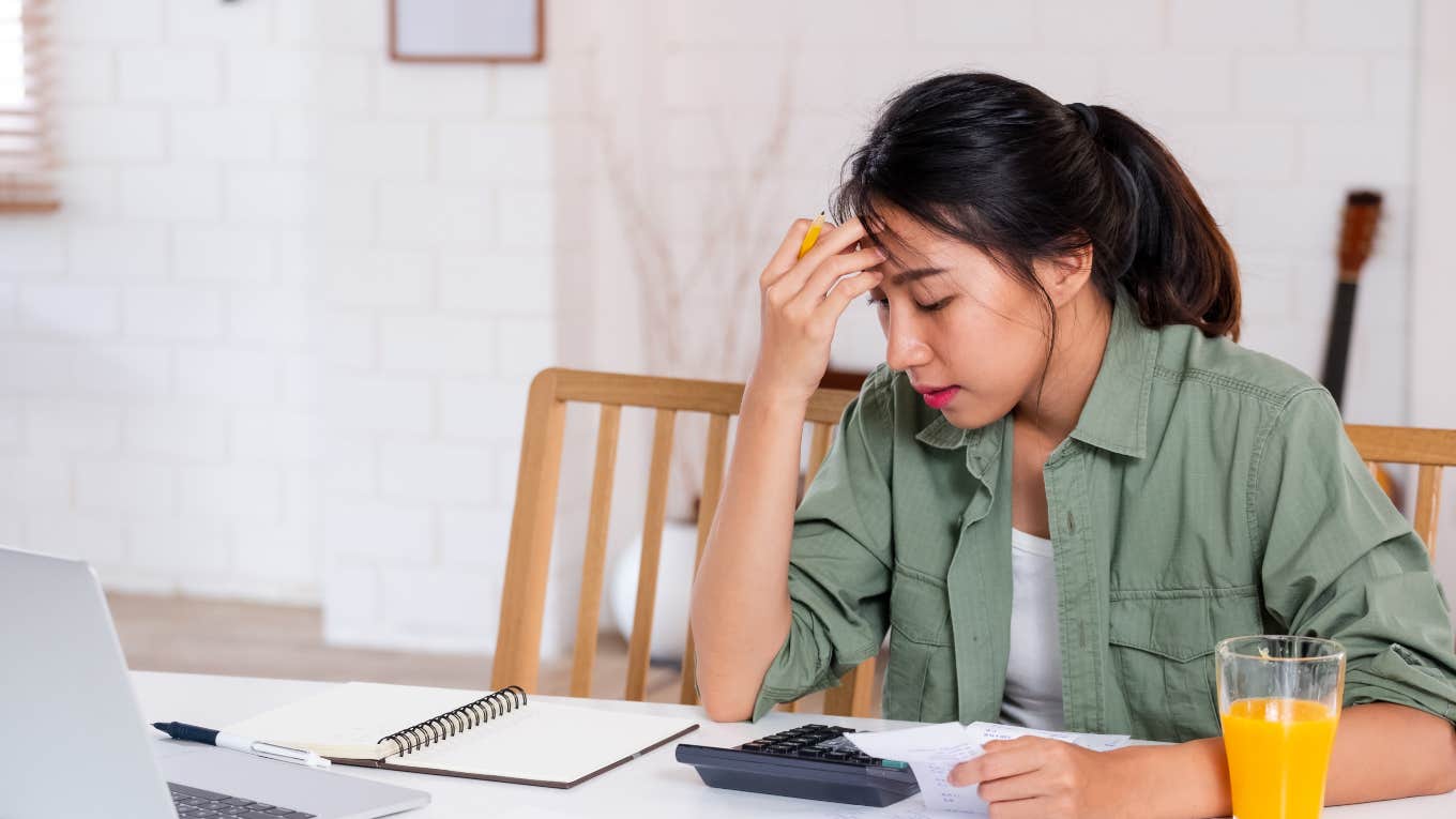 Millennial Realizes She'll Never Have Same Financial Stability As Her Parents woman sitting at kitchen table frustrated over budget