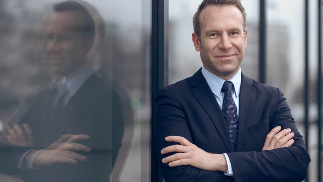 male businessman in blue suit and necktie with grin leaning on window outdoors