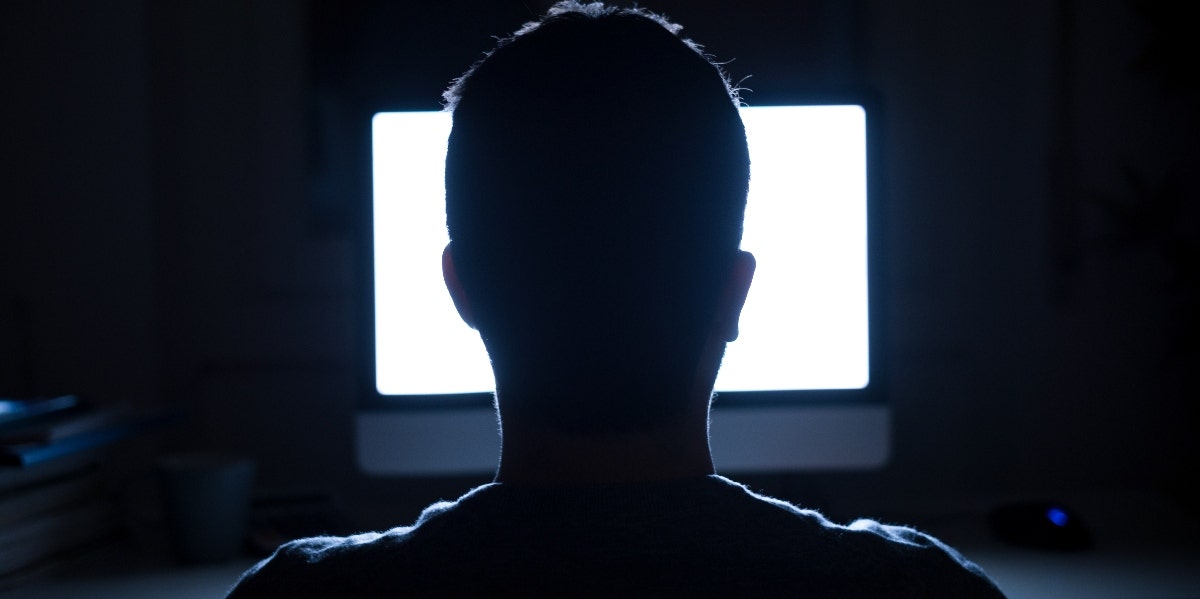 silhouette of man sitting in front of a lit computer screen