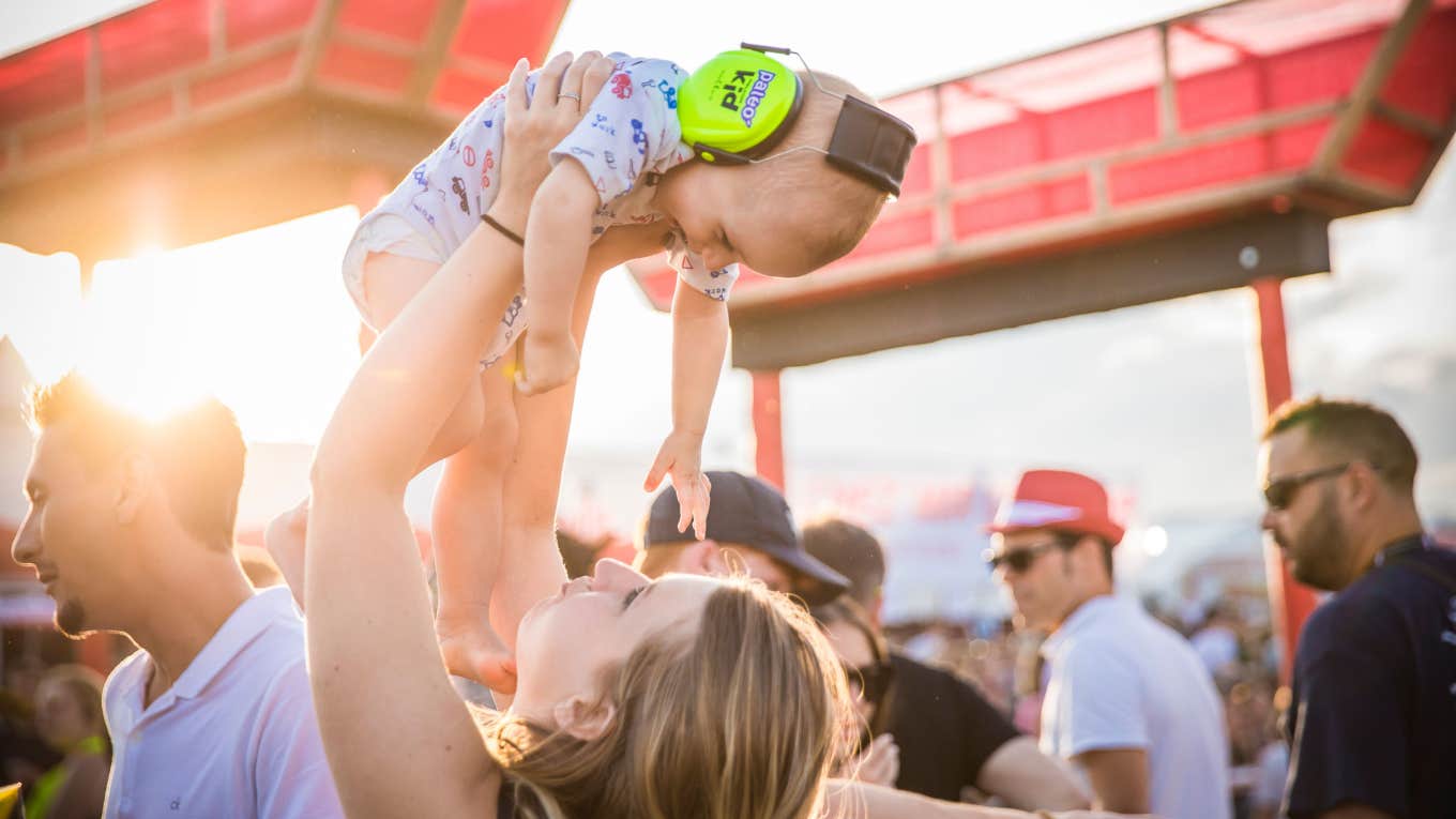 woman holds her baby wearing headphones during a music festival