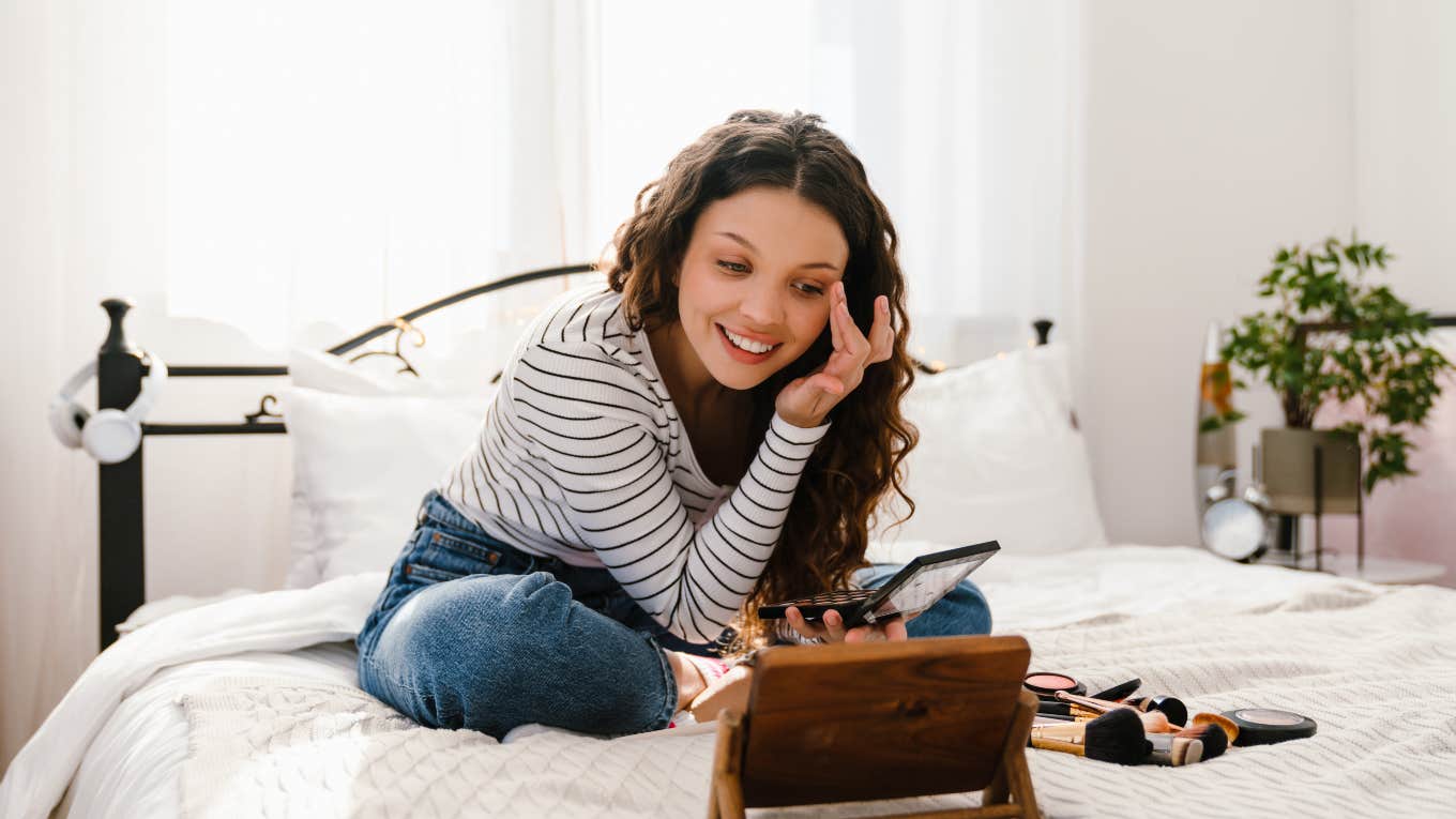 teenage girl sitting on bed doing her makeup