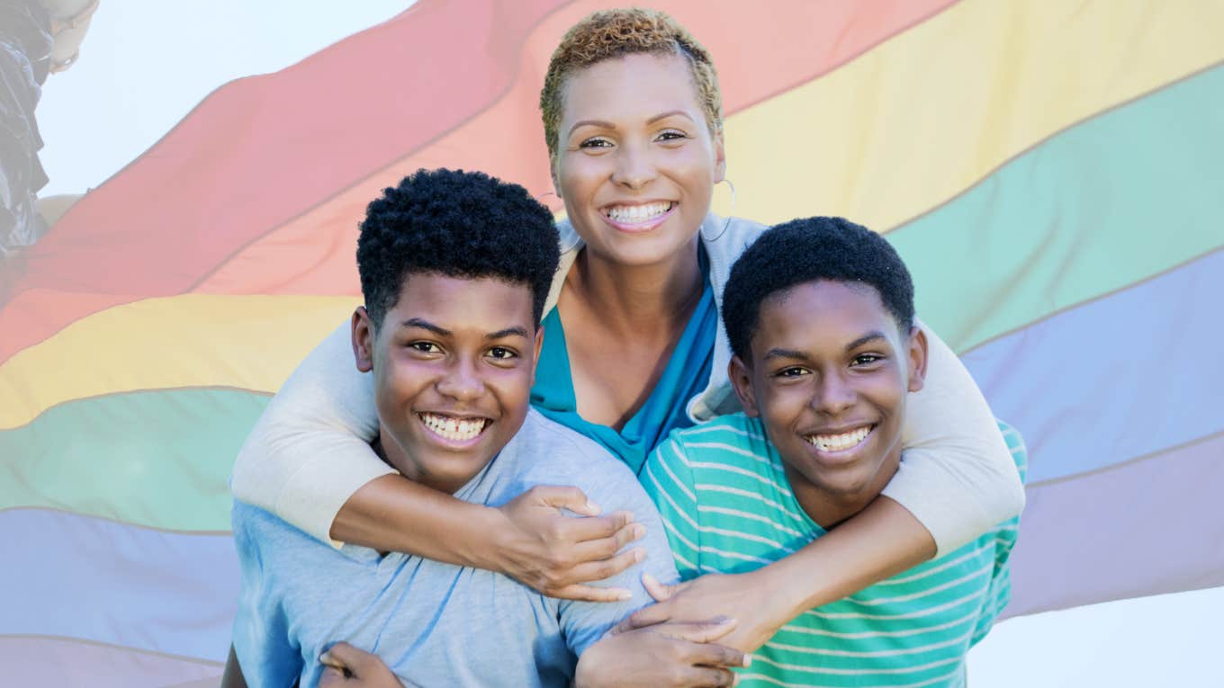 Mom hugging her Gen Alpha sons in front of rainbow flag. 