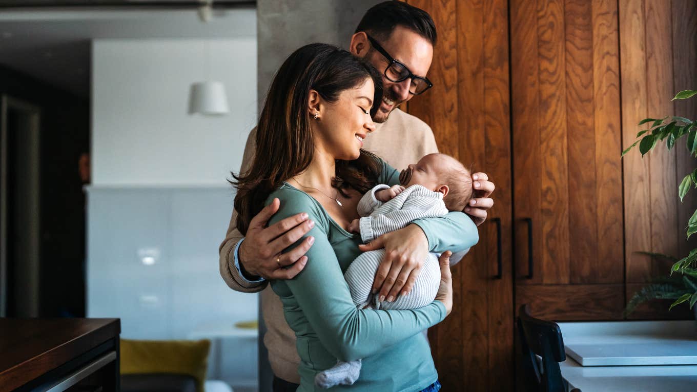 Portrait of young mother and father smiling while holding newborn baby in their home
