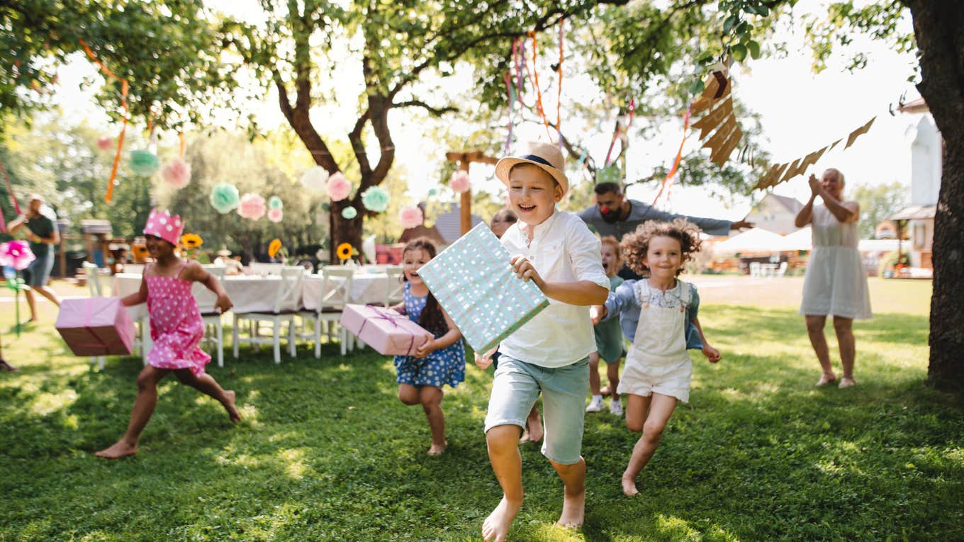 Small children running with present outdoors in garden on birthday party.