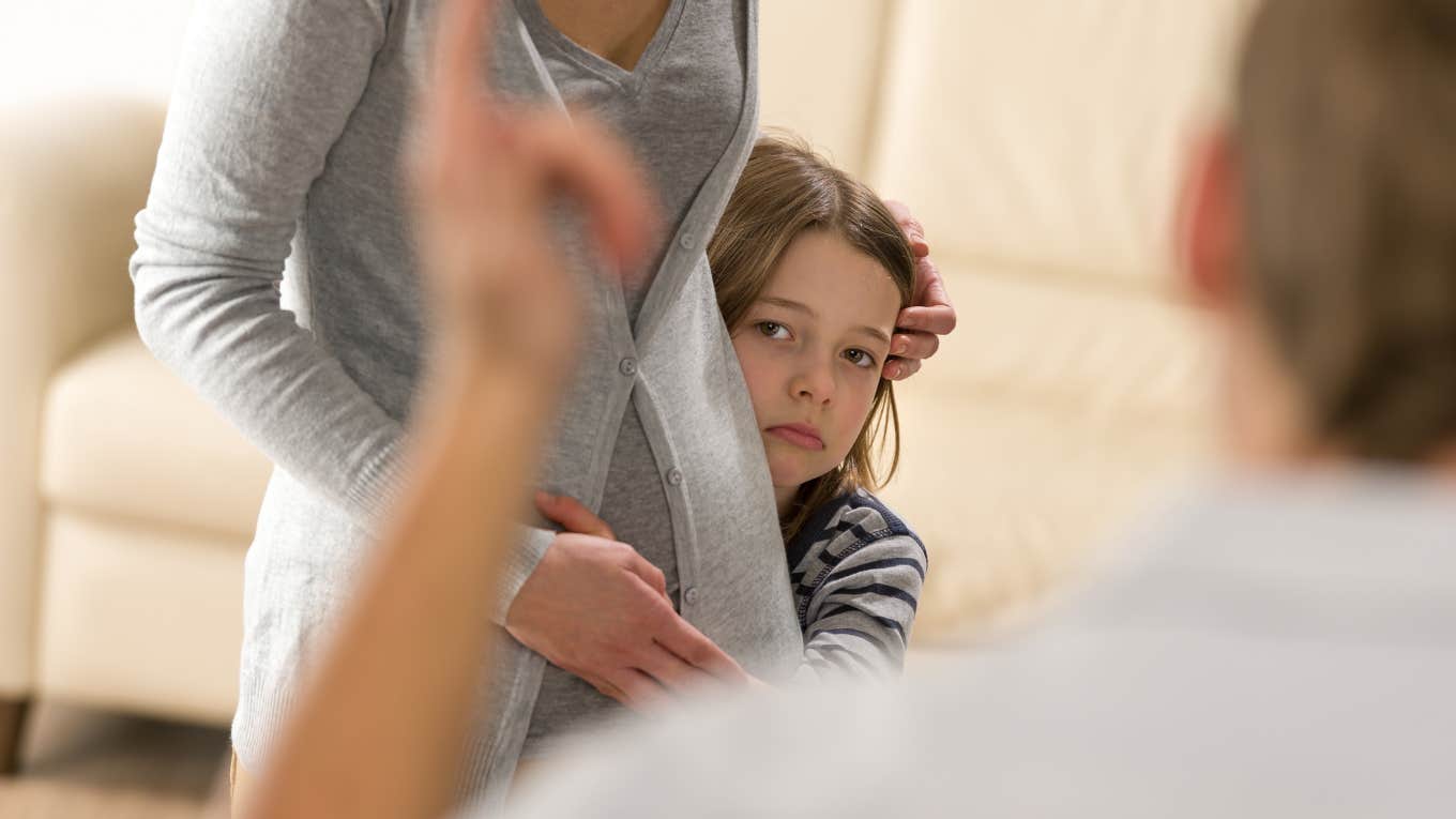 Scared little girl hiding behind mother from stepfather