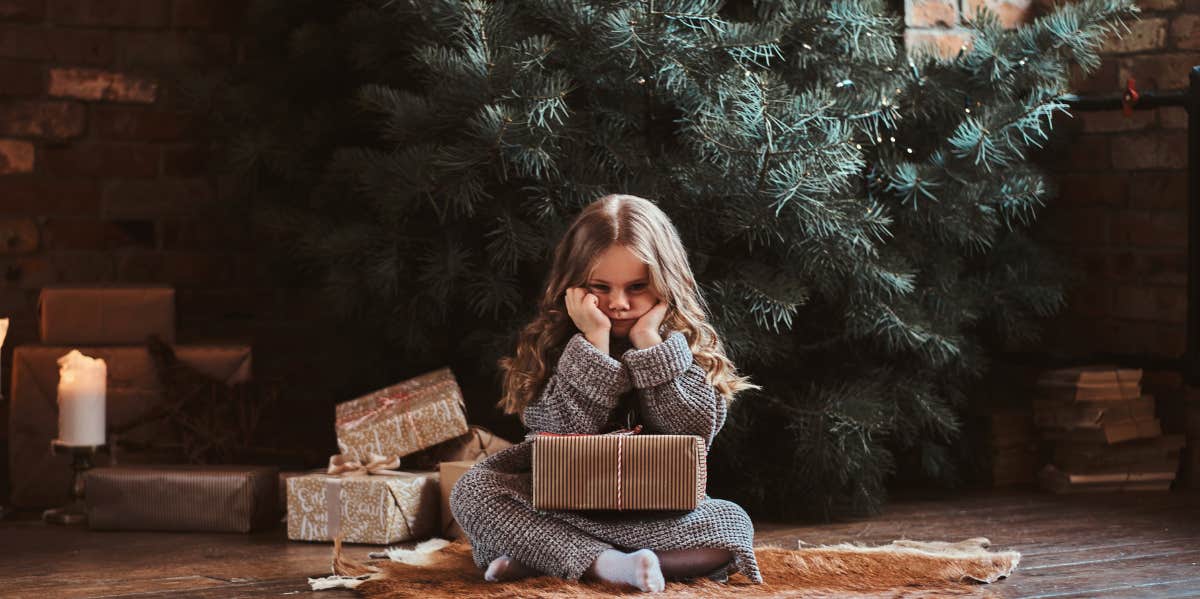 Sad kid sitting in front of an undecorated Christmas tree
