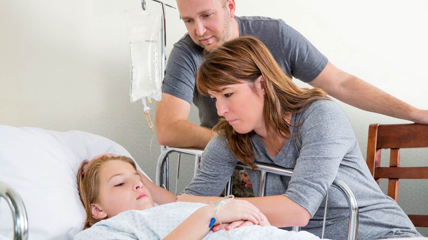 Mom and dad looking over their daughter in a hospital bed. 