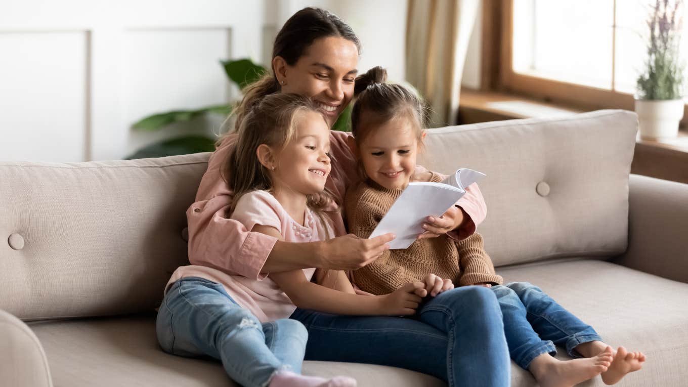 mother sitting on couch with two daughters and reading book to them