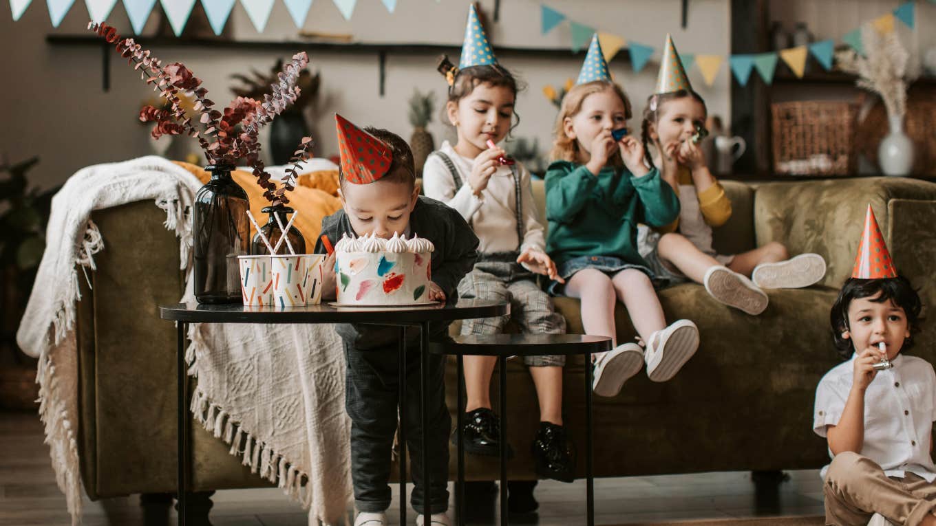 Mom Admits She's Done Throwing Birthday Parties For Her Kids After Spending $718 For 2 Hour Party little boy biting into birthday cake while children sit behind him at birthday party
