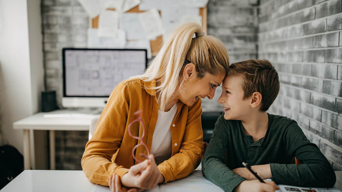 mom and son smiling at each other while touching foreheads and sitting at a desk