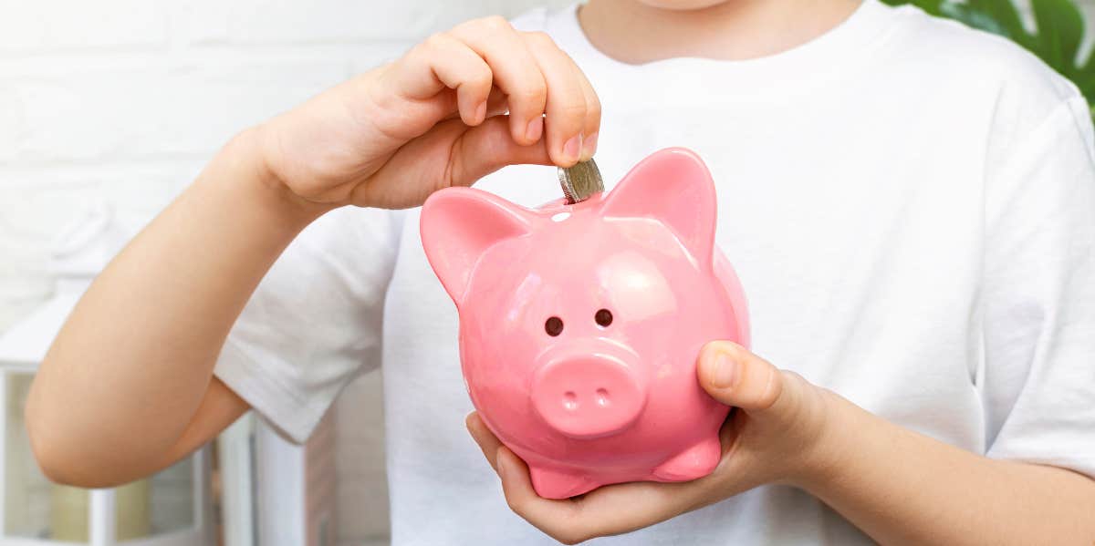 A child slips a coin inside a pink piggy bank.