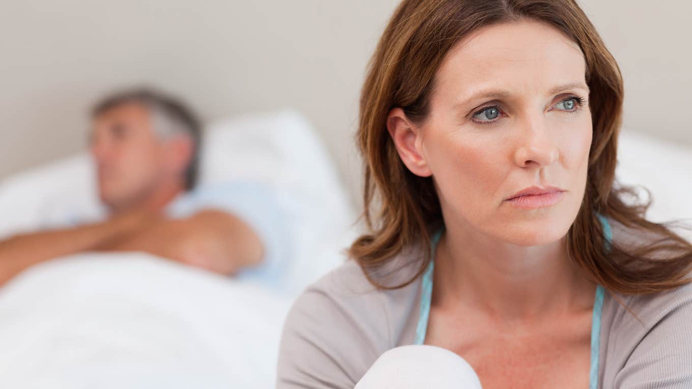 Sad mature woman on bed with her husband in the background