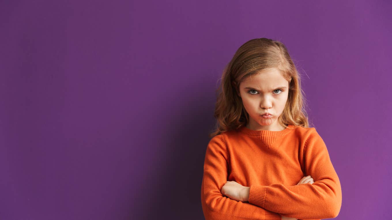 Mom Wonders If She Should Make Her Six-Year-Old Apologize angry little girl in front of purple backdrop