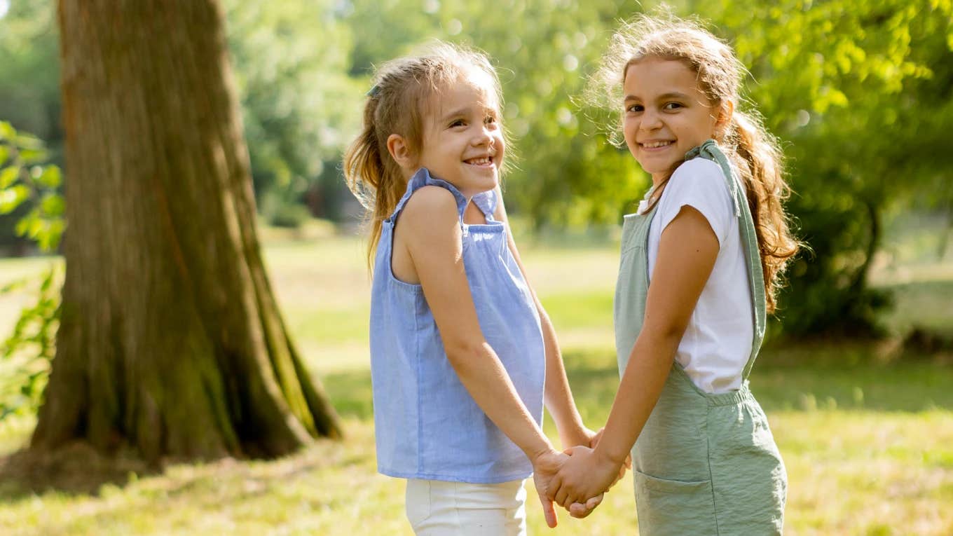 two young girls hold hands together outside