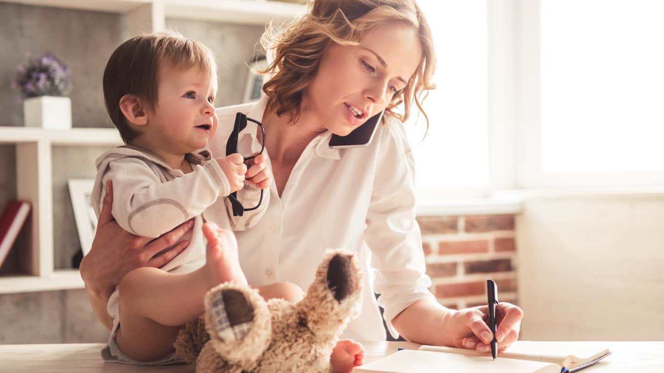 mom talking on the phone and taking notes while holding baby in arms