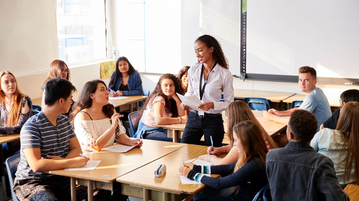 High School Teacher Standing By Student Table Teaching Lesson