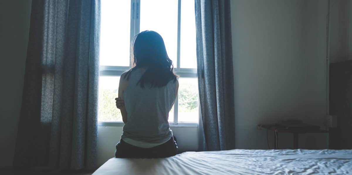 woman sitting on bed looking out window