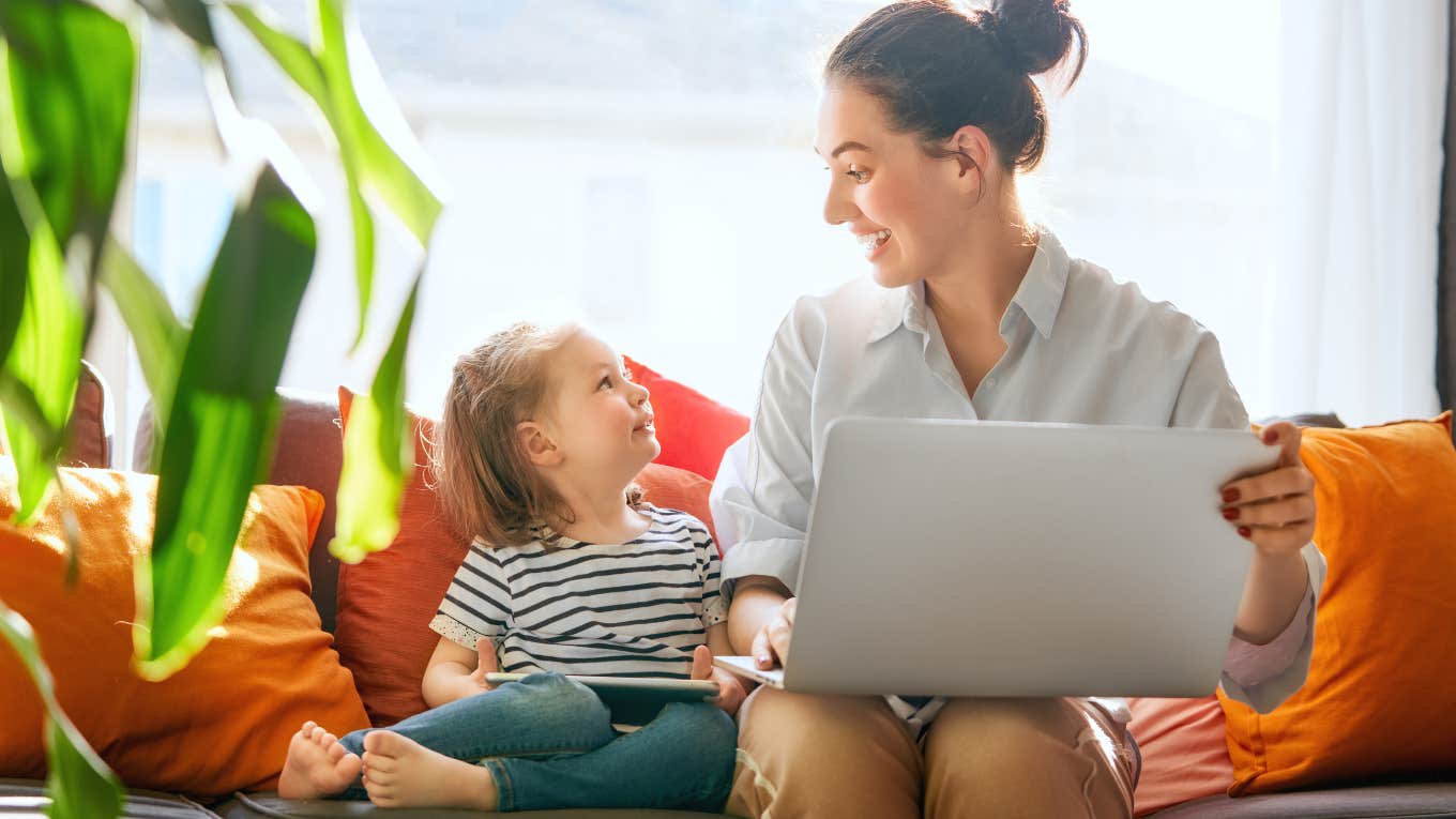 Mom working while her daughter sits next to her on the couch