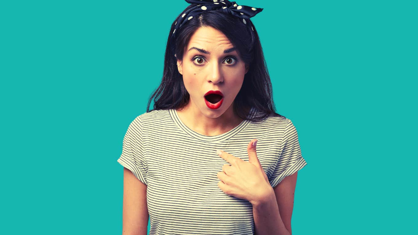 confused young beautiful woman dressed in striped top staring at camera with jaw dropped, pointing at herself