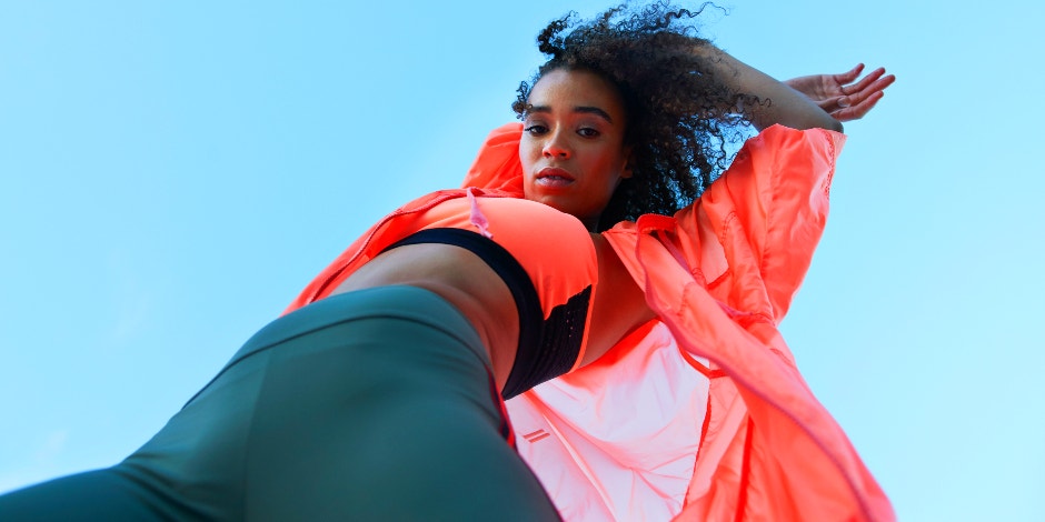 upward-facing shot of a young athletic Black woman in an orange top