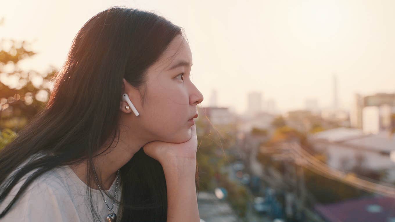 A young woman sits on a rooftop while listening to music