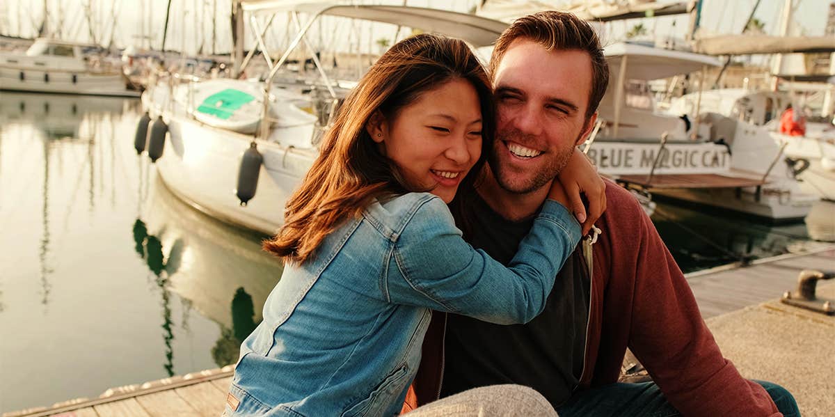 woman hugging man while sitting on dock