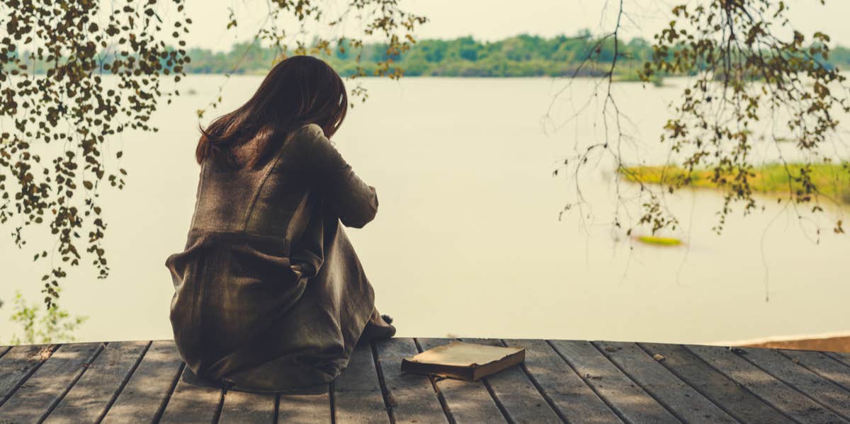 woman sitting by water holding her knees