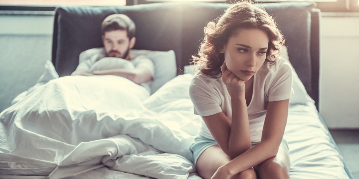 woman sitting on bed with man behind her