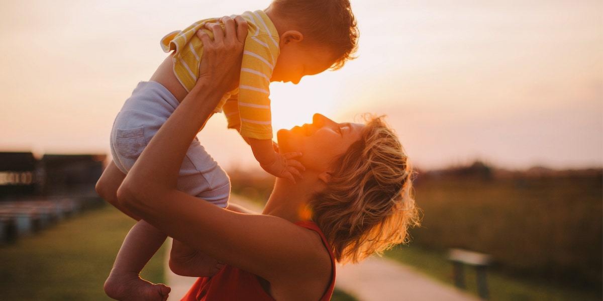 mom holding up baby with sunset in background