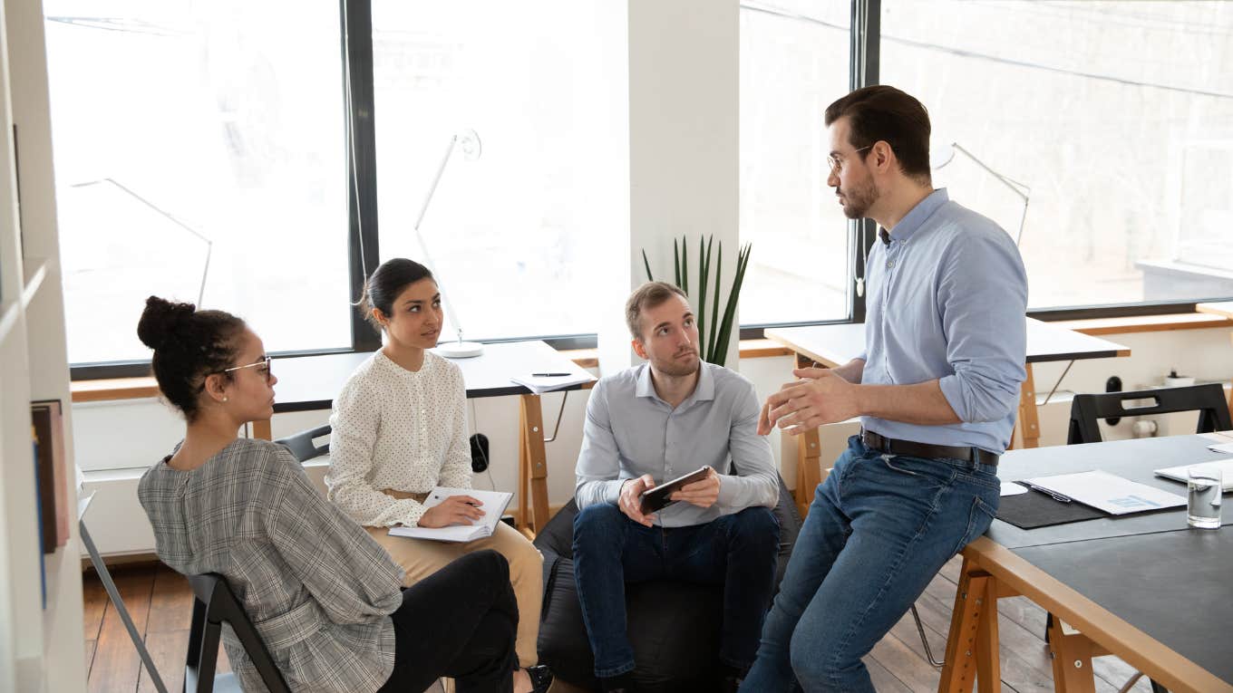 colleagues sitting on chairs listening to male boss in modern office