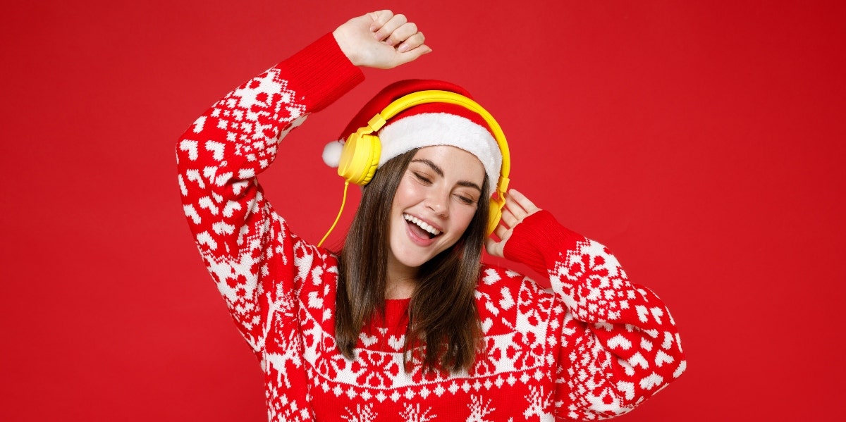 30 Obscure Christmas Songs That Are So Underrated woman dancing in christmas sweater and headphones