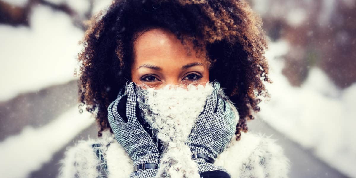 black woman with natural hair in the snow, scarf over mouth, big brown eyes look at camera
