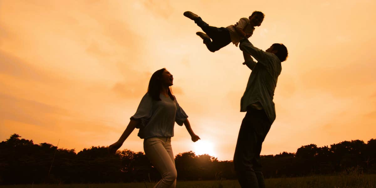 silhouette of two parents playing with child 