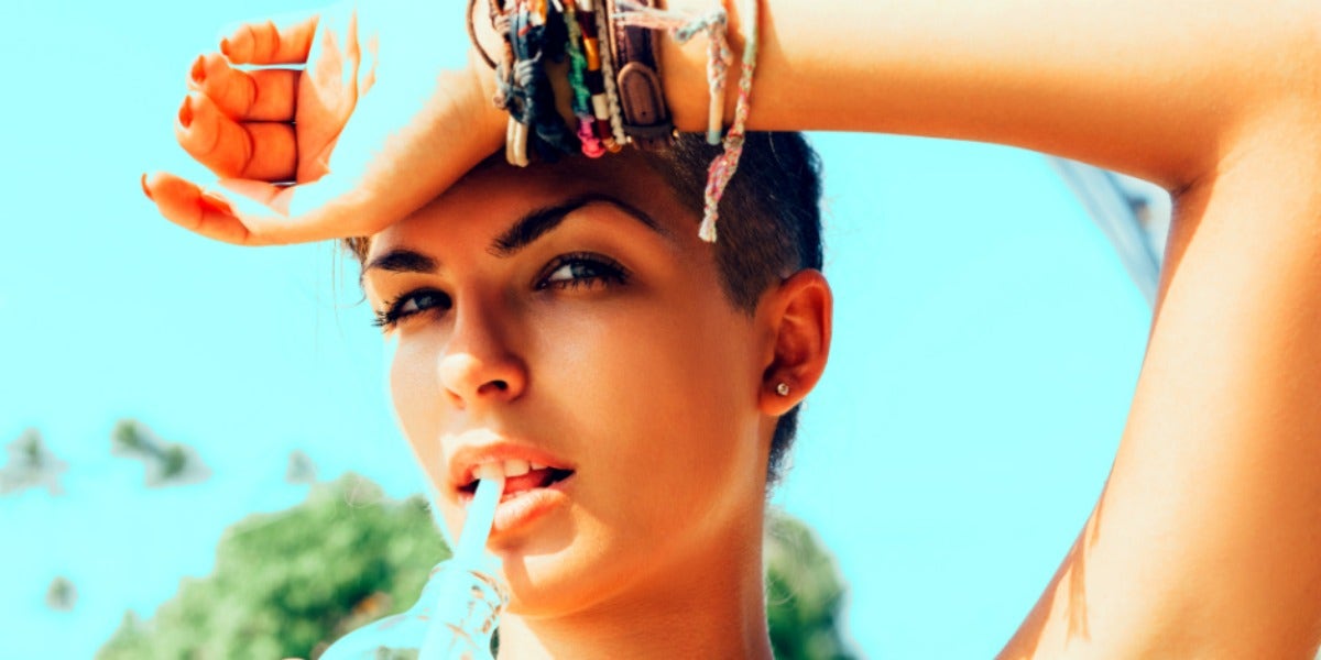 brunette woman against a blue background with her wrist to her forehead, looking into the camera