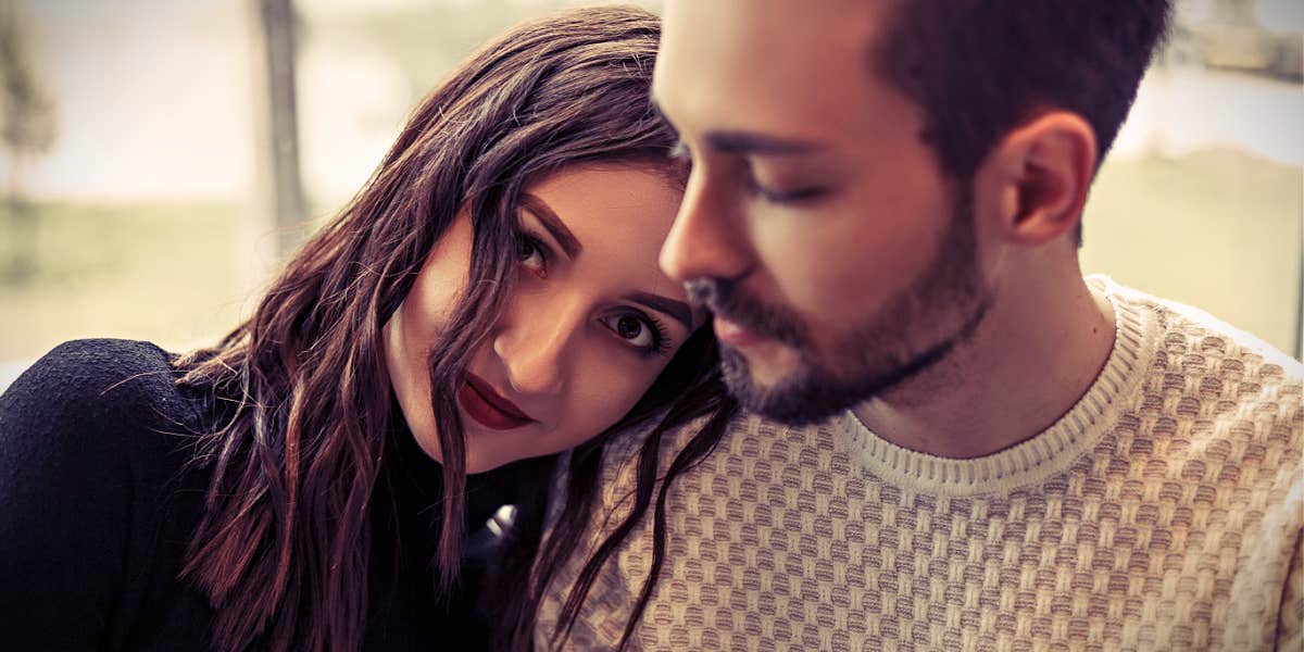 Woman with dark hair rests head on shoulder of a man who looks away