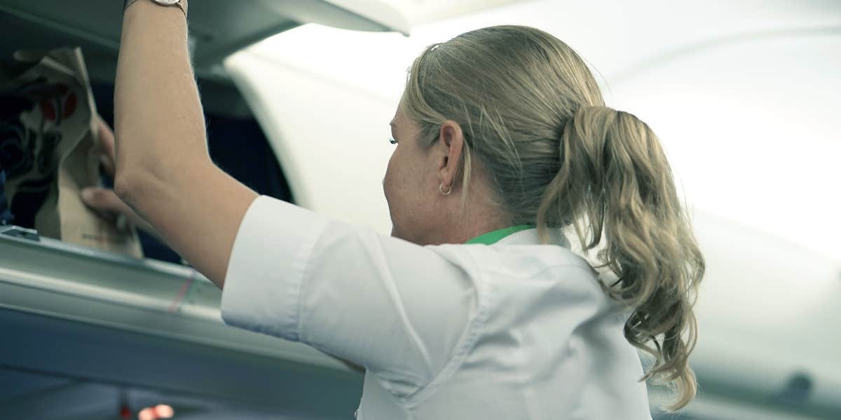 A flight attendant puts luggage in the overhead bin.