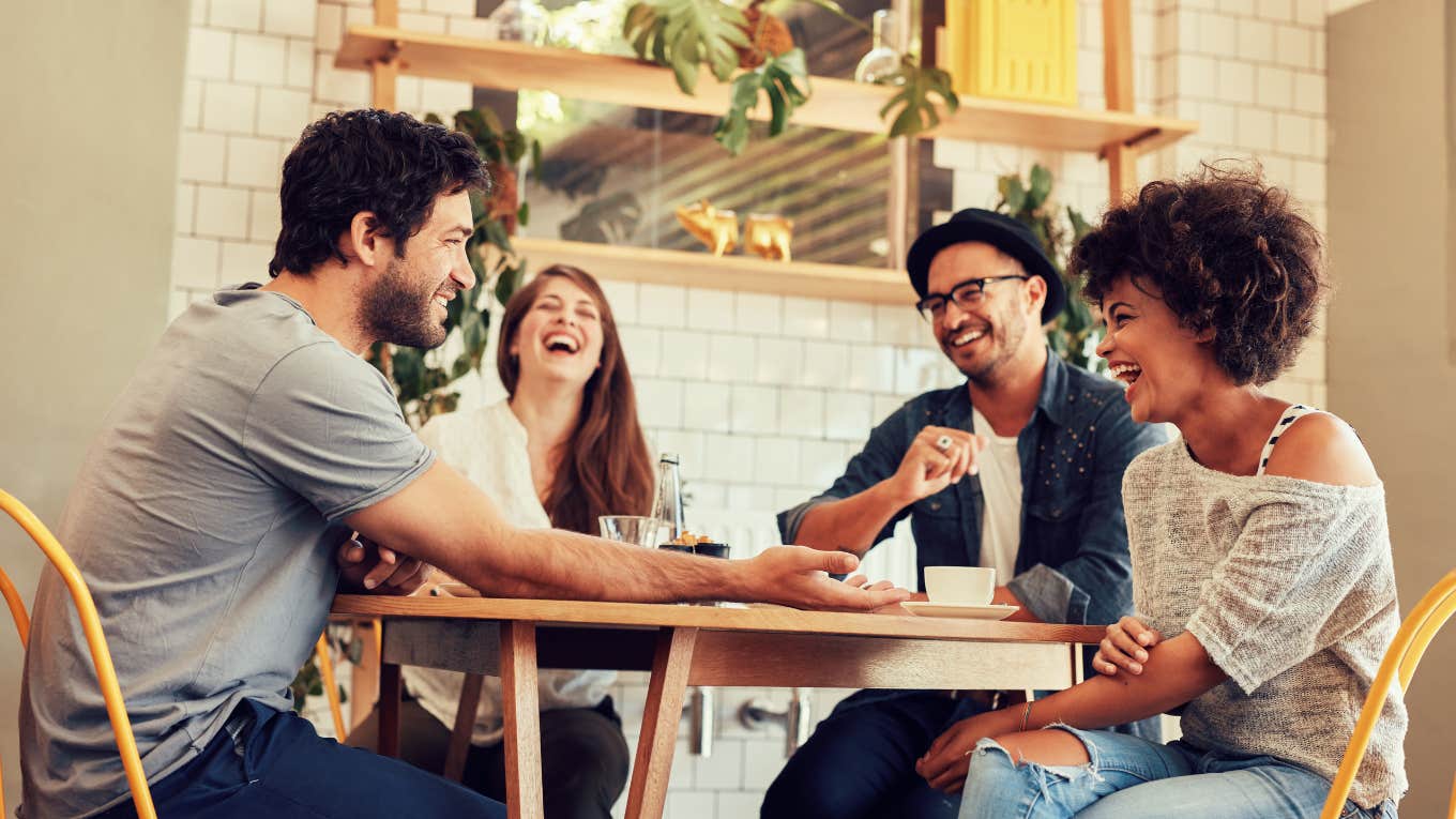 group of young friends laughing while sitting at table in restaurant 