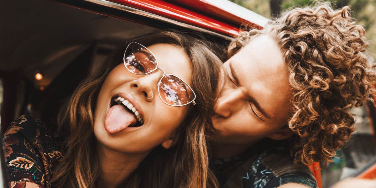 young couple with heads outside a red car being silly