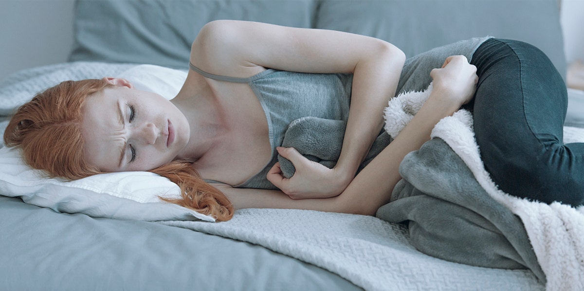 The Age You Got Your Period Can Predict How Long You'll Live woman in bed with menstrual cramps