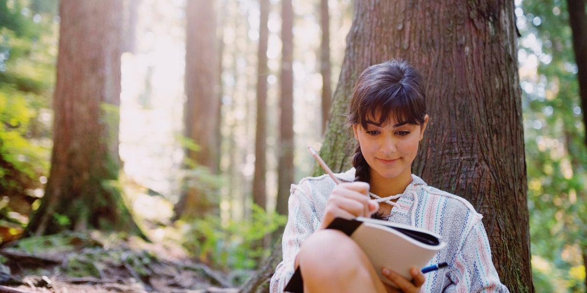 woman writing in a notebook under a tree