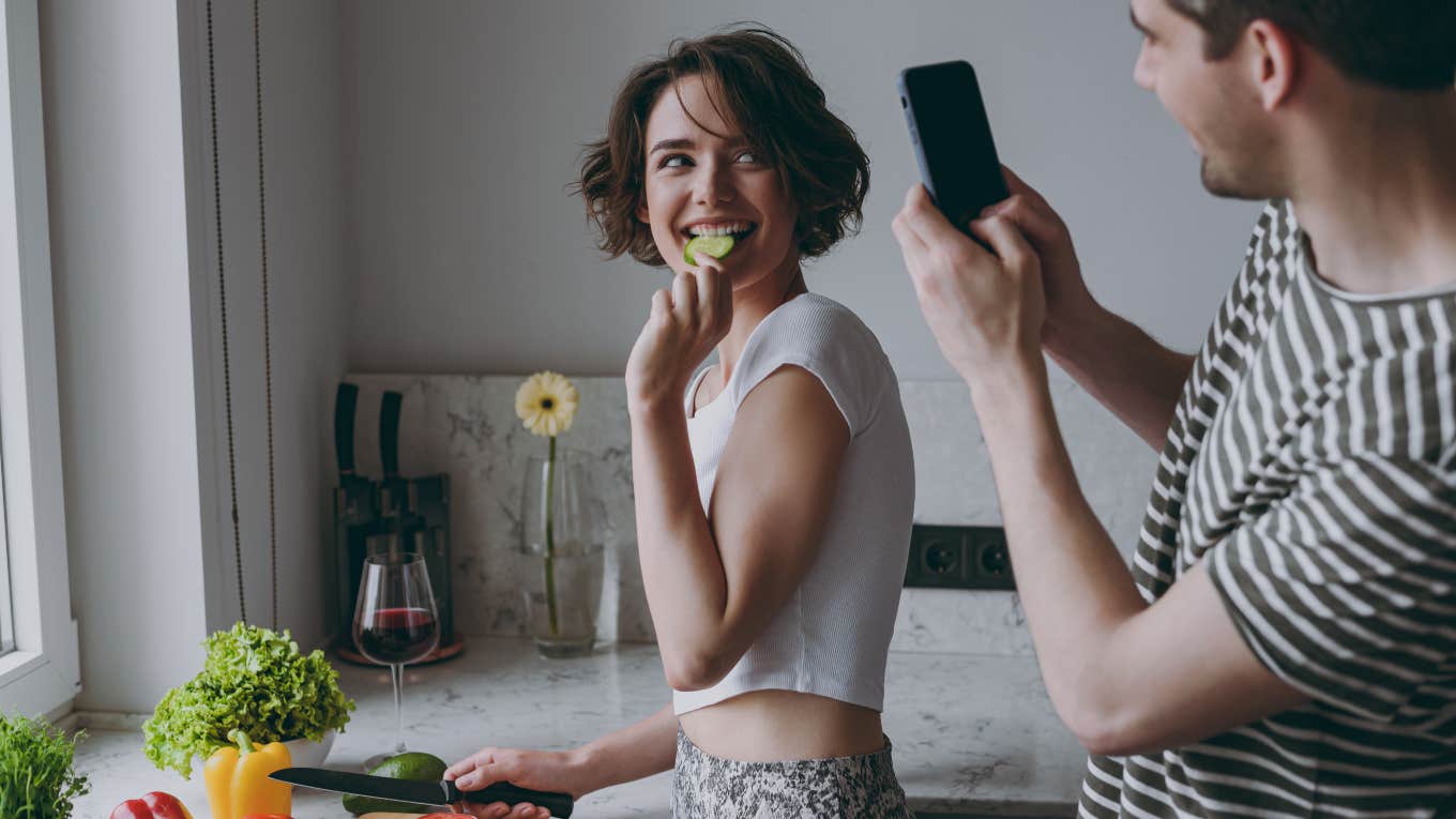 man taking picture of woman eating in kitchen