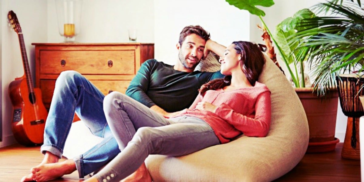 Pregnancy After Miscarriage: When To Try Again couple lounges in the sunlight, resting on a large pouf chair, looking at one another