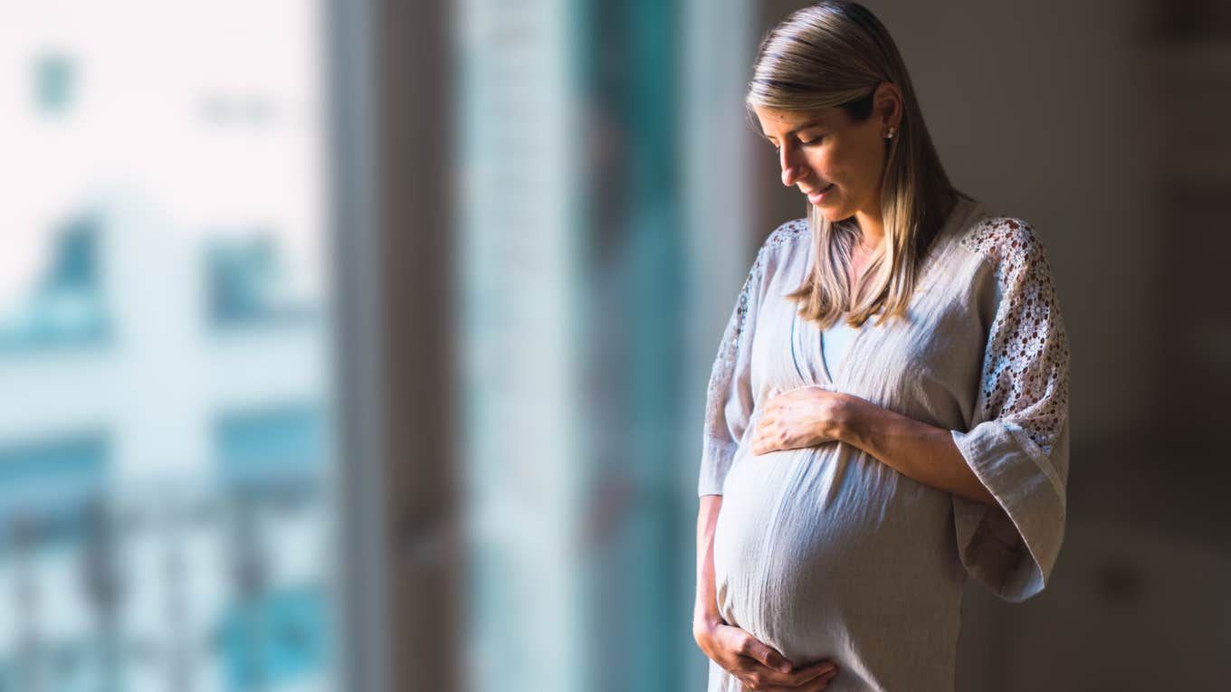 Pregnant woman looking solemn while looking at her belly. 