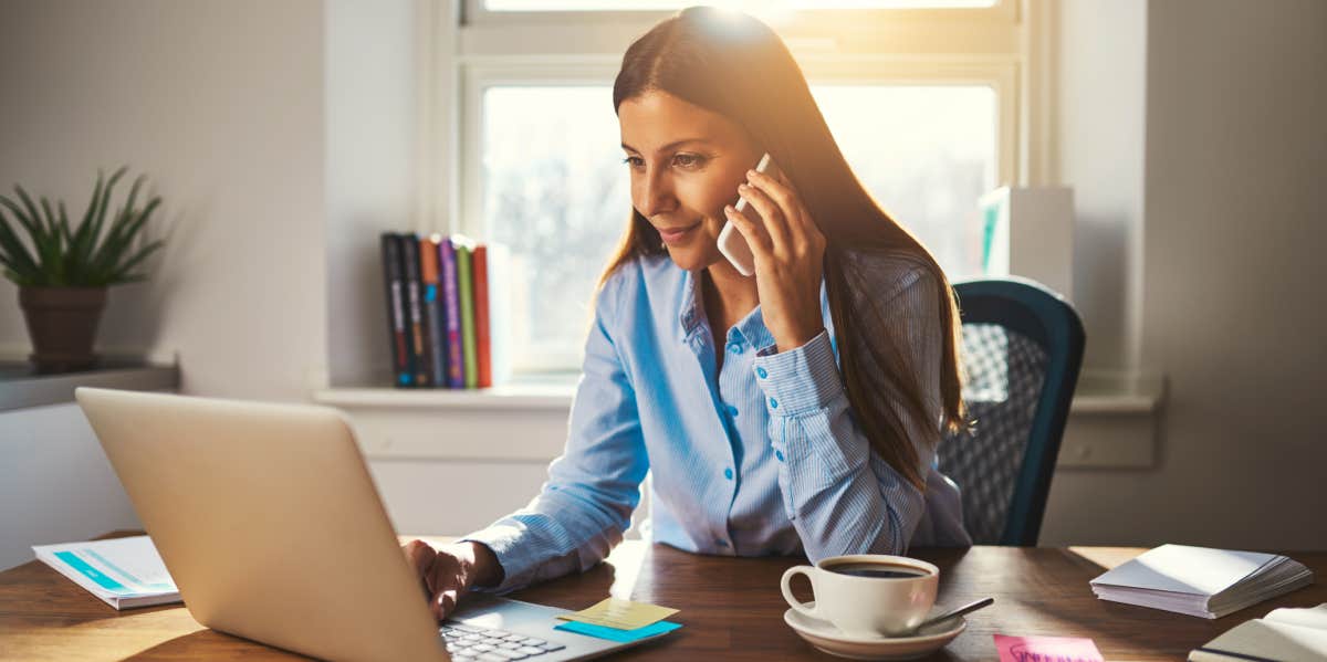 Woman working on laptop at office while talking on phone