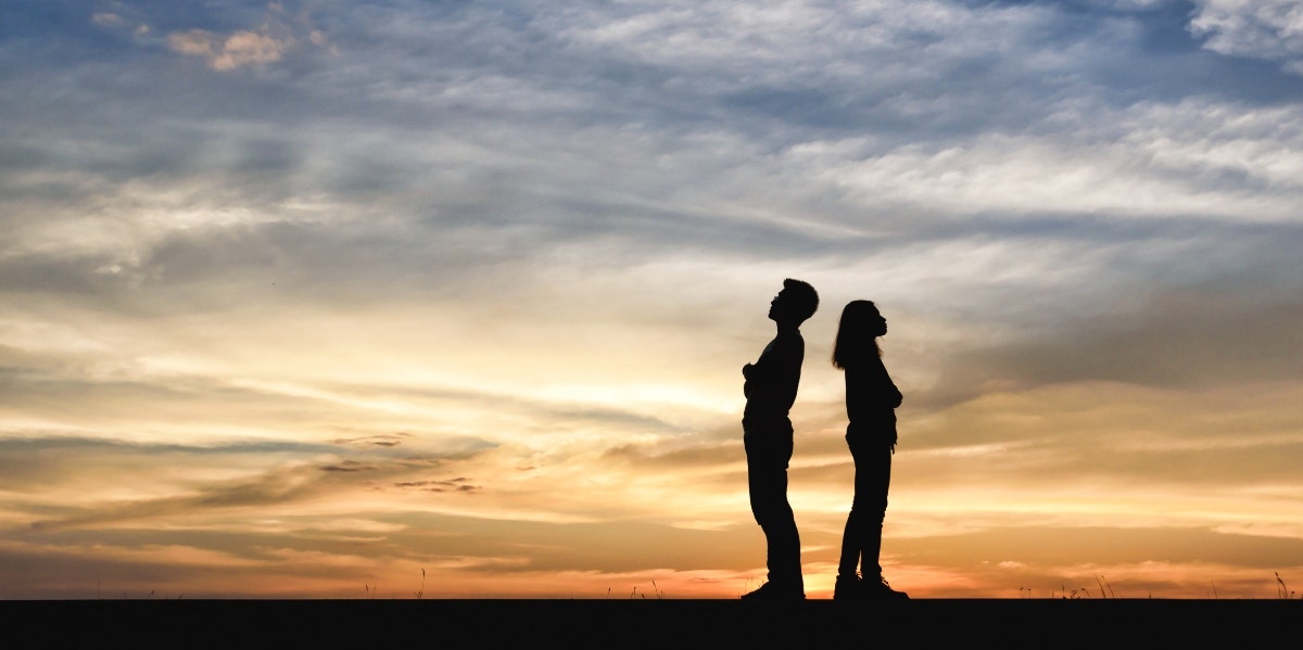 silhouette of couple standing back to back in front of sunset
