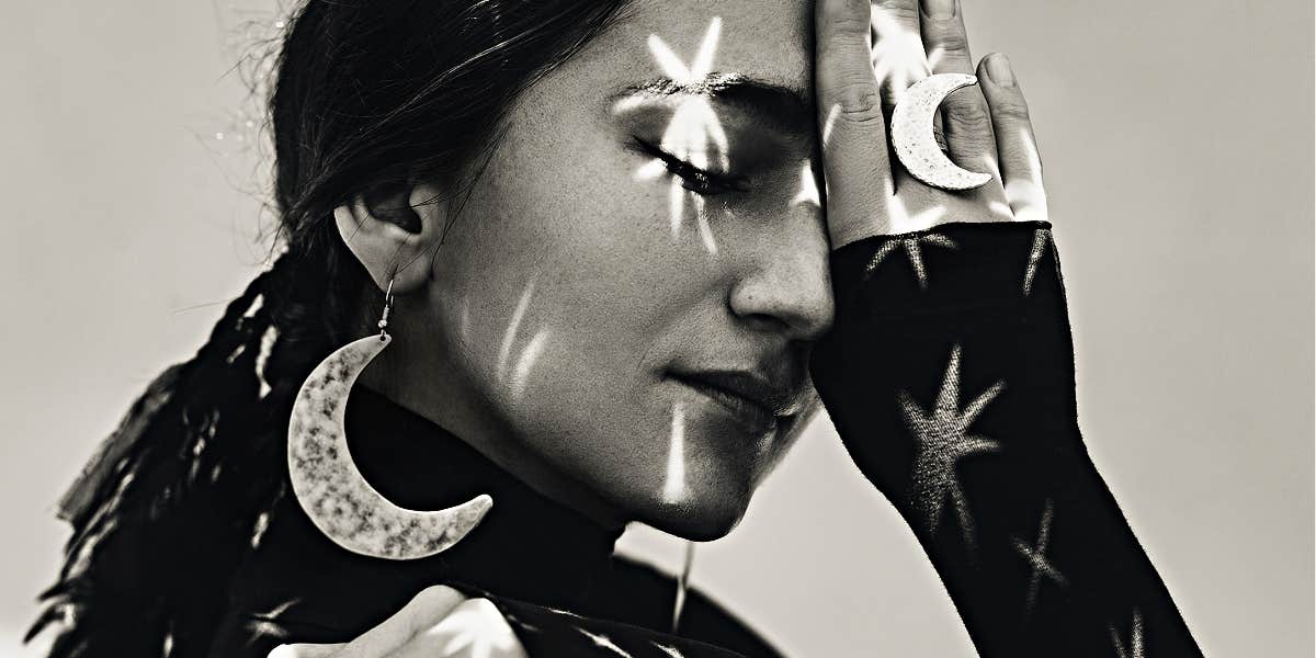 black and white image of a woman in moon earrings with stars projected on her face