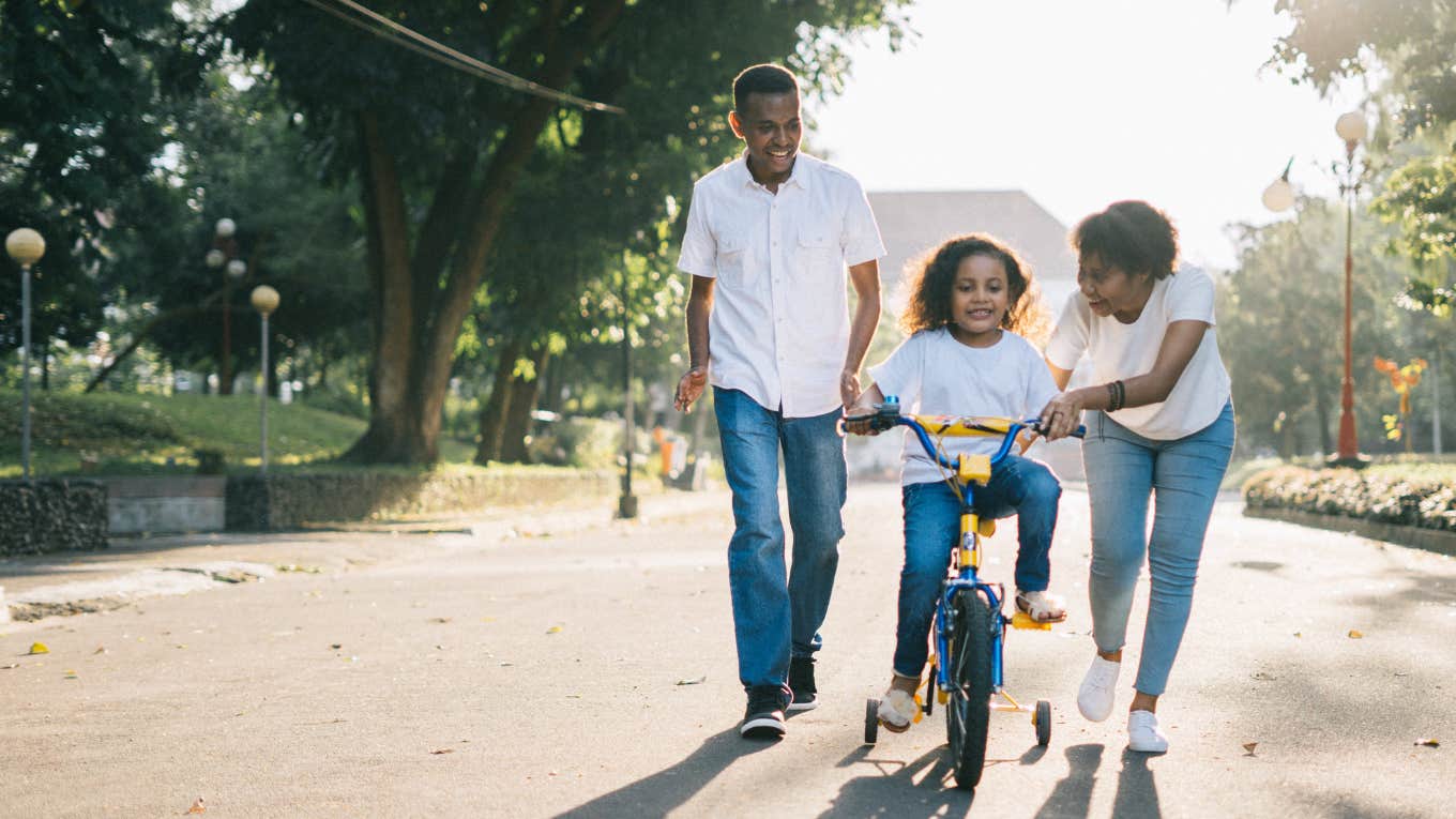 parents teaching kid to ride a bike 
